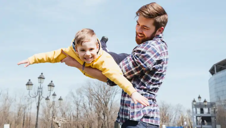 Young smiling father and his little son playing together in a city park