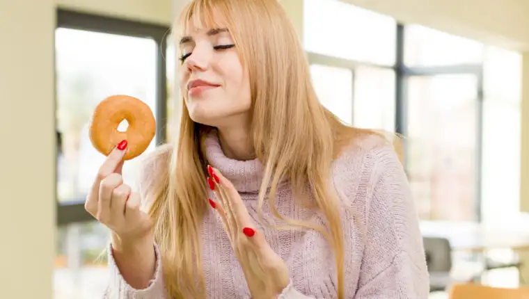 young pretty woman with a donut. unhealthy diet concept at home interior