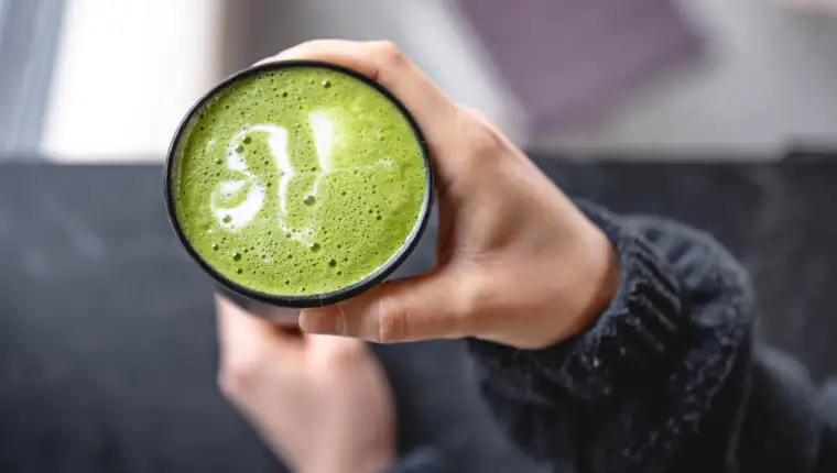 Cup of Matcha Green Tea in woman hand, top view.
