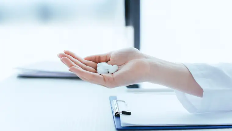 cropped shot of doctor with handful of pills near clipboard on table