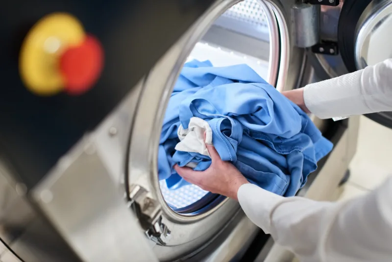 Hands loading laundry into washing machine in dry cleaning