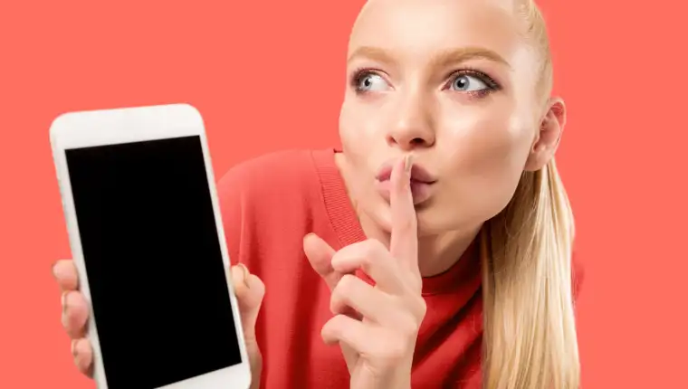 Portrait of a confident casual girl showing blank screen mobile phone isolated over coral background