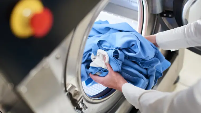 Hands loading laundry into washing machine in dry cleaning