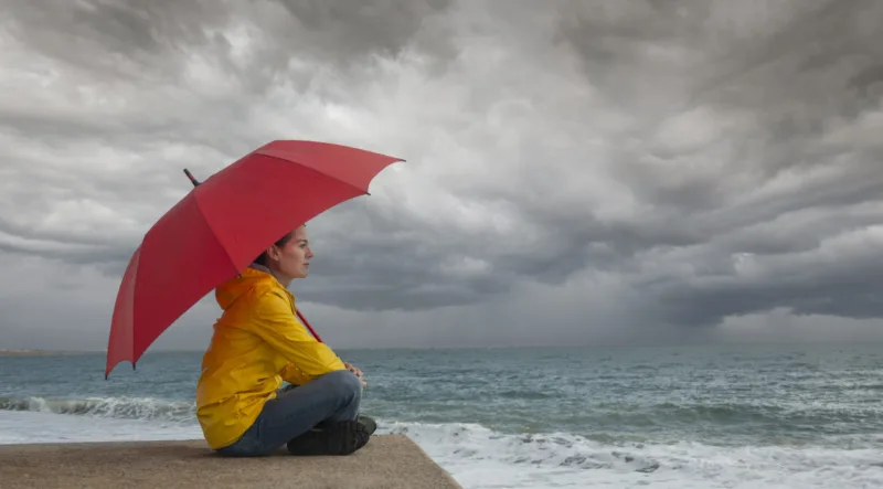 Woman with red umbrella watching storm clouds over the ocean, st