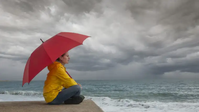 Woman with red umbrella watching storm clouds over the ocean, st