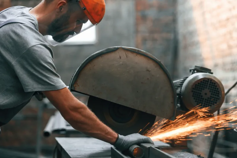 Focused work cutting metal young man factory grey uniform