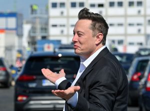 ljudska prava na Twitteru Elon Musk vlasnik Twittera na ulici u crnom sakou i bijeloj košulji uslikan iz profila raširio ruke i smije se u pozadini ulica automobili i zgrade vedar dan