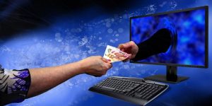 jedanaest osoba uhapšeno internet prevare ruka uzima novvac iz ruke koja izlazi iz računara ilustracija plava pozadina iza crni ekran sa tastaturom sivom