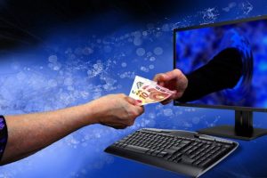 jedanaest osoba uhapšeno internet prevare ruka uzima novvac iz ruke koja izlazi iz računara ilustracija plava pozadina iza crni ekran sa tastaturom sivom