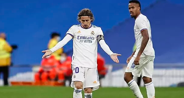 Real našao zamjenu za Modrića Luka Modrić na utakmici Reala u bijelom dresu, sa trakom na kosi, bijele štucne pored njega Militao iza dva redara travnjak i plave tribine