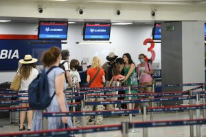 Haos na aerodromu u Beogradu odgođeni letovi ljudi sa maskama njih desetak čekaju u redu ispred šaltera za ckeck-in u majicama kratkih rukava vidi se koridor za putnike na plazma ekranima piše Air Serbija