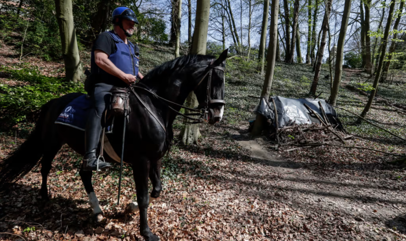Policajac na konju ide kroz šumu gdje spavaju migranti u šatorima