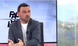 Magazinović u studiju Face TV sivi sako bijela majica gestikulira rukama iza njega plazma ekran piše Face TV
