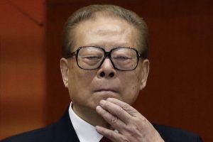 Bivši kineski predsjednik Jiang Zemin crni sako bijela košulja crna kravata crne naočale drži ruku na bradi iza bordno zid polutamna prostorija