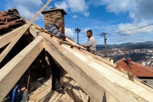 na Širokači je u subotu izgorio krov kuće radnici popravljaju krov stavljaju nove grede u daljini se vidi grad kuće u mahalama plavo nebo dimnjak