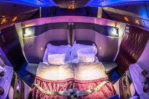 najluksuznije aviokompanijedupli krevet u avionu sa dva jastuka i roze prekrivačima preko prekrivača sigurnosni pojas roze naslonjač iznad kreveta plava svjetla udobna atmosfera i čisti luksuz