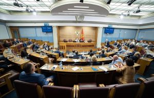 Crnogorski parlament zasjeda stolovi i stolice poredani u polukrug i okrenuti prema jednom stolu u vrhu prostorije za kojim sjede predsjedavajući parlamenta i zamjenici ukrašen svod bijeli zid plav na stolovima bijeli papiri plave fascikle crnogorska zastava