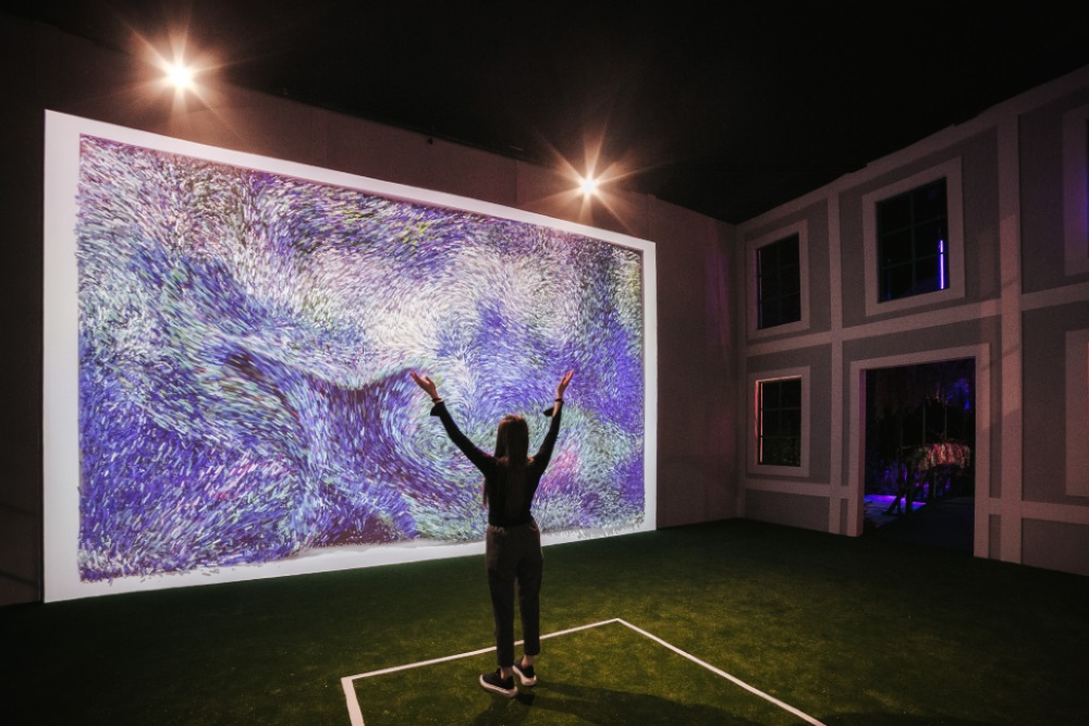 Monetova djela izložena u Beču najsavremenijom digitalnom tehnologijom djevojka odjevena u crno i tenisice stoji leđima okrenuta ruku dignutih uzrak i raširenih ispred nje veliki plazma ekran sa slikom umjetnika zeleni pod kao trava ona stoji u bijelo opcrtanom kvadratu zagušena svjetlost