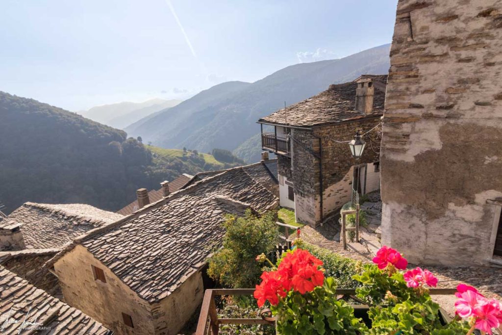 Odsječeni od ostatka Italije selo Monteviasco u Lombardiji kuće nakrcane jedna na drugu u brdu okolo drveće zeleno kuće sa sivim krovom djeluju staro vedar dan cvijeće crveno i roze na balkonima