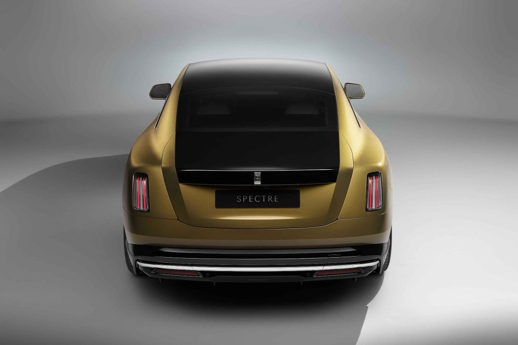 Rolls-Royce novi model Spectre automobil zlatne i crne boje crna boja na dijelu prednje haube i prati liniju preko krova koji je potpuno crn i gepeka siva podloga iza automobila kao da je u prostoriji