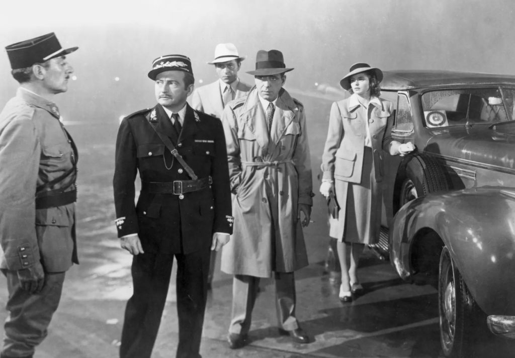 Casablanca crnobijela scena iz filma Ingrid Bergman i Humphrey Bogart stoje na ulici okolo magla pored njih dva policajca iza jedan muškarac i sa desne strane automobil