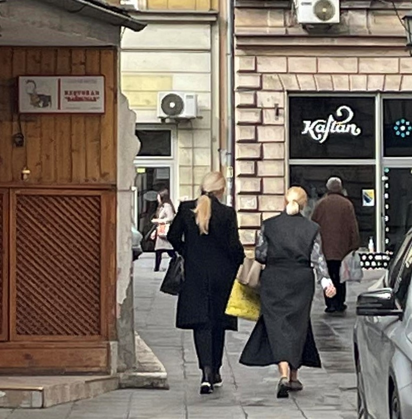 bahatost režima Sebija Izetbegović slikana s leđa sa još jednom ženskom osobom hoda ulicom na ćaršiji u crnim jaknama i prslucima duge plave svezane kose nose kese u rukama
