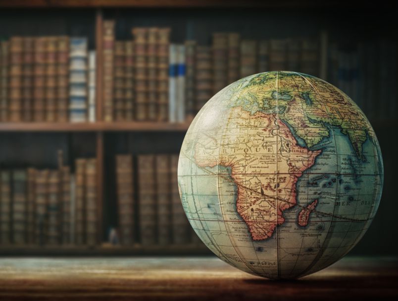 Listenbourg globus sa geografskom kartom svijeta u polumraku iza police sa knjigama kao u biblioteci globus na drvenom stolu