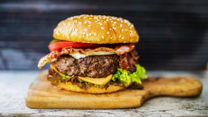 po čemu je hamburger dobio ime sočan hamburger na drvenoj daski sa sirom lukom paradajzom zelenom salatom na sivom stolu tamna pozadina iza