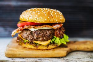 po čemu je hamburger dobio ime sočan hamburger na drvenoj daski sa sirom lukom paradajzom zelenom salatom na sivom stolu tamna pozadina iza