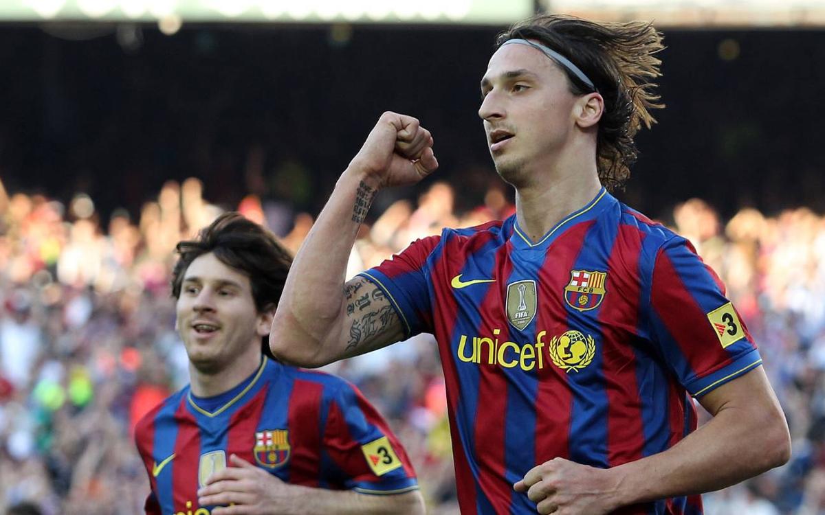 Ibrahimović u dresu Barcelone na terenu slavi sa desnom rukom podignutom u zrak i stisnutom pesnicom duga kosa zakačena rajfom tetovaže u pozadini se vidi Messi