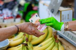 Godišnja stopa inflacije u eurozoni prodaja banana na stolu žena daje 10 eura prodavačici koja nosi drečavo zelene rukavice iza se vide ljudi na pijaci dan na stolu banane