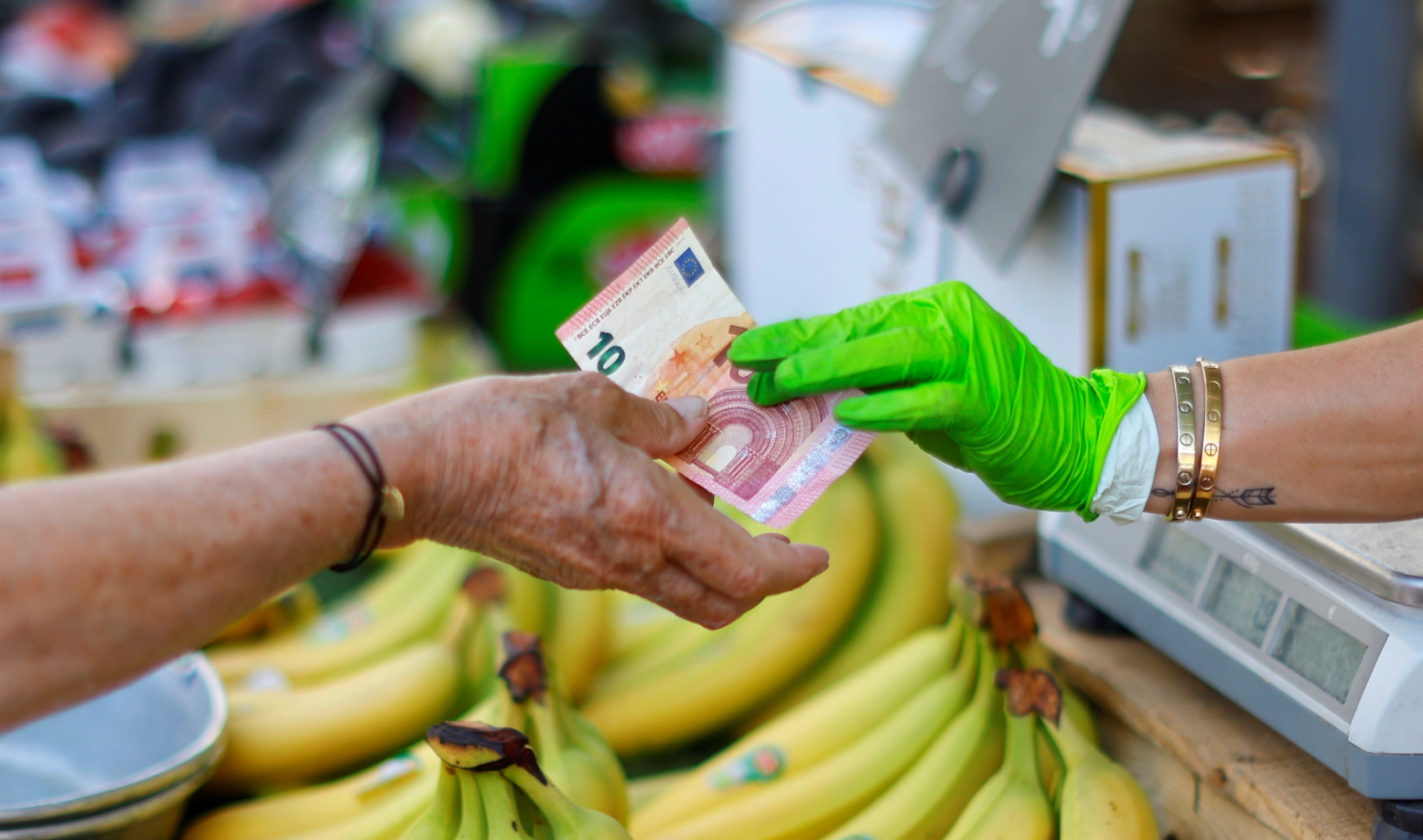 Godišnja stopa inflacije u eurozoni prodaja banana na stolu žena daje 10 eura prodavačici koja nosi drečavo zelene rukavice iza se vide ljudi na pijaci dan na stolu banane
