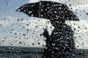 Vremenska prognoza za nedjelju kiša pada kapi kiše na staklu kroz staklo se nazire crna silueta žene koja nosi kišobran u daljini oblačno nebo
