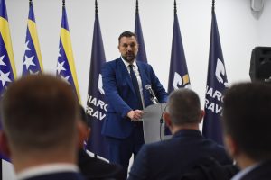 Konaković u Tešnju za govornicom iza njega zastave BiH ispred ljudi koji se vide s leđa dvorana