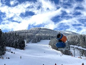 Bjelašnica i Igman spremni za skijašku sezonu top koji izbacuje snijeg na stazi na Bjelašnici narandžasto plave boje staza pod snijegom šuma pod snijegom sunčan dan nebo s malo oblaka