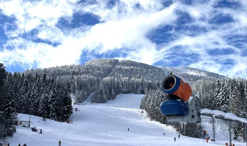 Bjelašnica i Igman spremni za skijašku sezonu top koji izbacuje snijeg na stazi na Bjelašnici narandžasto plave boje staza pod snijegom šuma pod snijegom sunčan dan nebo s malo oblaka