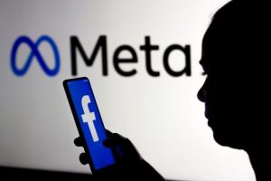 Meta planira velika otpuštanja žena drži mobitel sa facebook iza piše meta