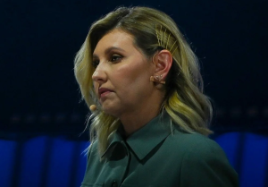 olena zelenska slikana iz profila u zelenoj košulji kosa duga plava stavljena iza uha iza tamno kao mrak ima mikrofon nakačen na uho prema ustima