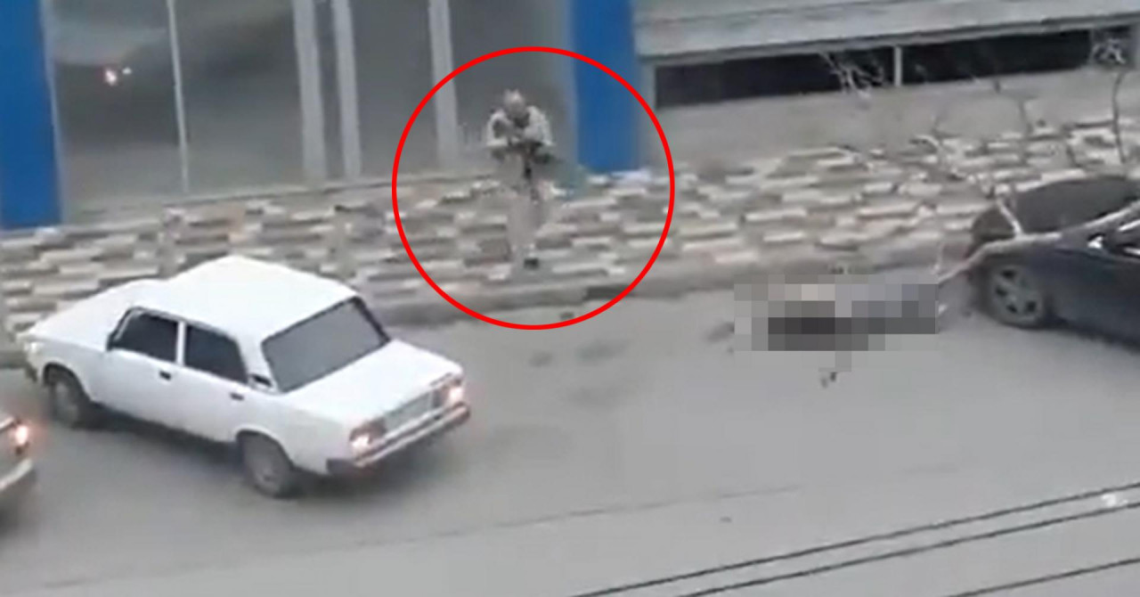uznemirujuća snimka muškarac u sivoj odjeći sa puškom u ruci na ulici na trotoaru pored njega bijeli automobil muškarac zaokružen crvenim krugom pored tijelo ubijenog koje je zamagljeno da se ne vidi