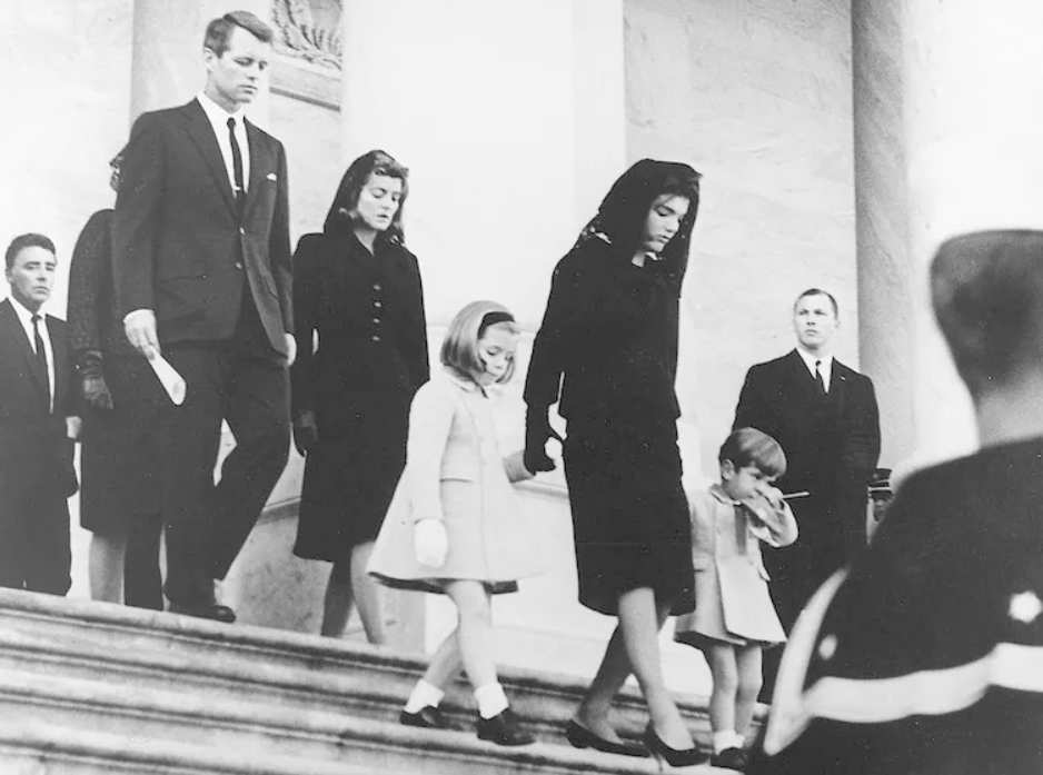 Jezive priče o slavnoj dinastiji Kennedy Porodica Johna F. Kennedyja kreće na sahranu žena u crniji  sa djecom ide niz stepenice iza muškarac i žena u crnini