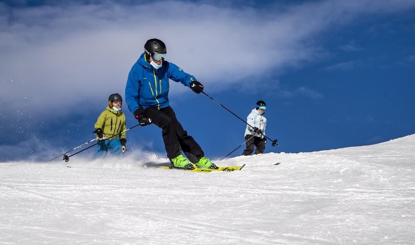 Inflacija ubija zimsku sezonu tri skijaša na stazi snijeg plavo nebo skijaš prvi u plavoj jakni crnim hlačama zelene skije iza u bijeloj i žutoj jakni
