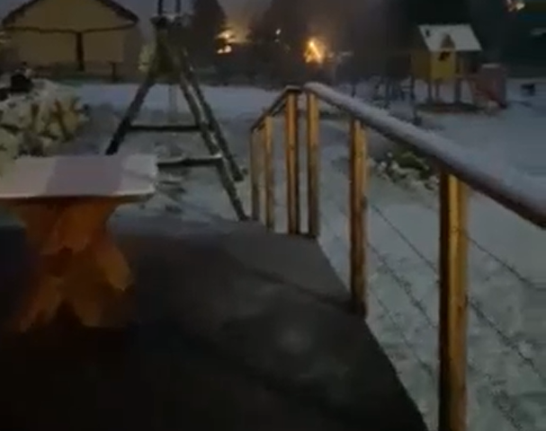 snijeg noćna fotografija ograda i pod ispred vikendice snijeg pao po stolu i po ogradi i na ulici u daljini se vide svjetla planina Vlašić