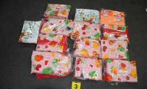 krijumčarenje kokaina na tamnoj podlozi 12 platnenih stolnjaka upakovanih u providne vrećice pored njih oznaka brojem tri crvena roze narandžasta cvjetići i voće