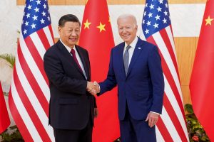 sastanak Bidena i Xija na Baliju lijevo Xi u crnom odijelu i bijeloj košulji bordo kravata desno Joe Biden u tamnoplavom odijelu bijela košulja šarena kravata obojica se smiju iza po dvije američke i kineske zastave u bijela podloga vidi se cvijeće rukuju se