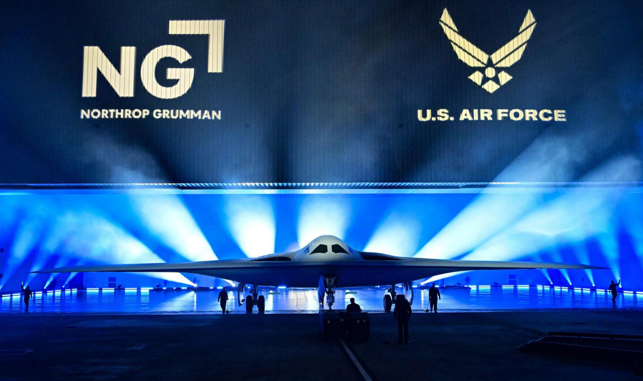 ‘nevidljivi‘ bombarder avion u ogromnoj hali na bini bijele boje iza njega svjetlost u snopovima plavičasta ispred voditelj ceremonije i nekoliko vojnika na slici grb US Air FOrce i u lijevom uglu velikim slovima NG