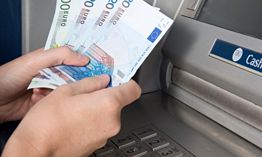 plaćanju karticom u obje ruke drži novčanice eura pored bankomata