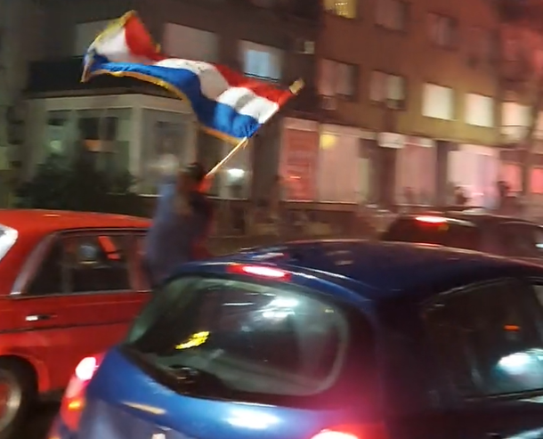 slavi se i u Mostaru momak viri iz automobila kroz prozor maše zastavom Hrvatske slavi pobjedu Hrvatske u Mostaru noć plavi i crveni automobil