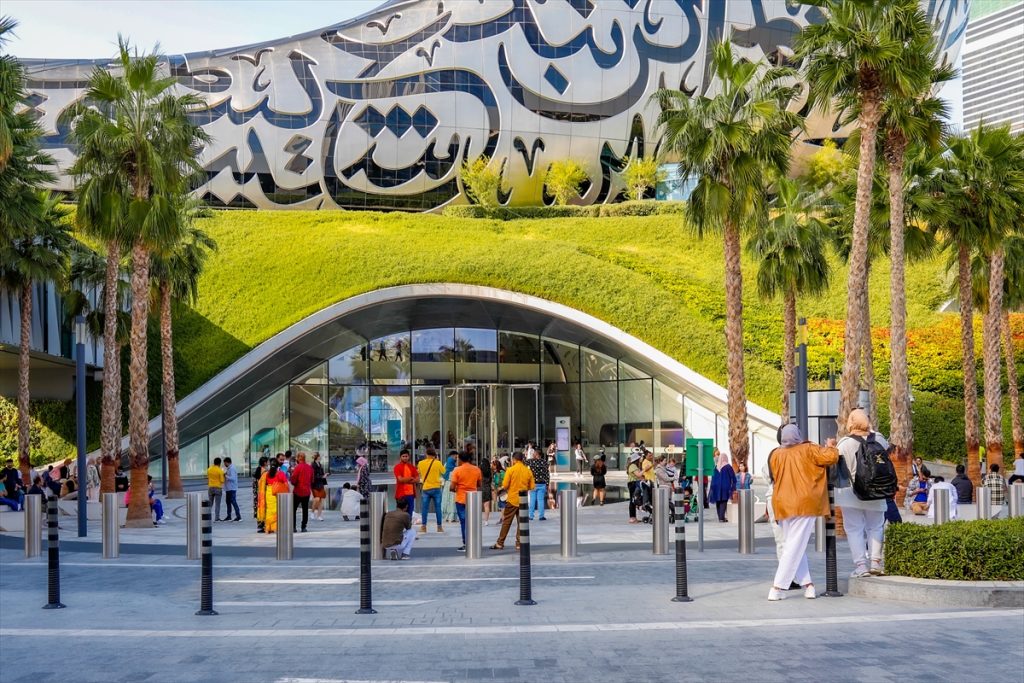 Dubai ljudi šetaju ispred spomenika ogromnog trava dan sunce