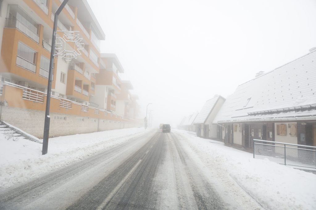 Zimska idila uz snježne pahulje sa lijeve i desne strane apartmani žuta fasada auto ispred neprohodna cesta